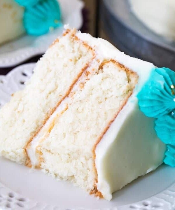 Slice of white cake with white icing and blue icing decorations on plate