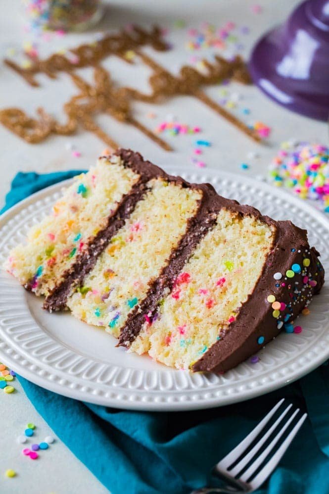 This is the BEST BIRTHDAY CAKE RECIPE! This vanilla cake is light and fluffy and packed full of colorful sprinkles! #birthdaycake #birthdayparty #easycakerecipe Slice of vanilla birthday cake on white plate