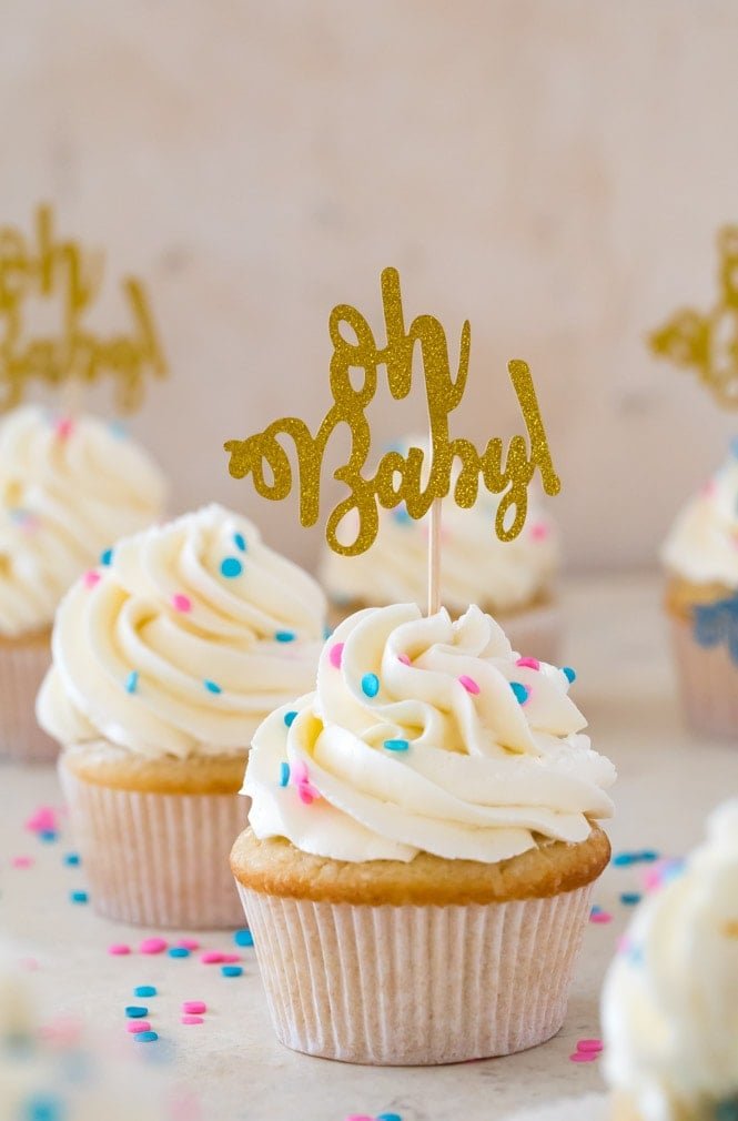 A sweet and simple recipe for Gender Reveal Cupcakes! Fill them with either pink or blue sprinkles for a fun surprise reveal #genderreveal #genderrevealcupcakes #genderrevealcake #babyshower #sugarspunrun Vanilla cupcake with white icing and blue and pink sprinkles and gold "oh baby" cupcake topper