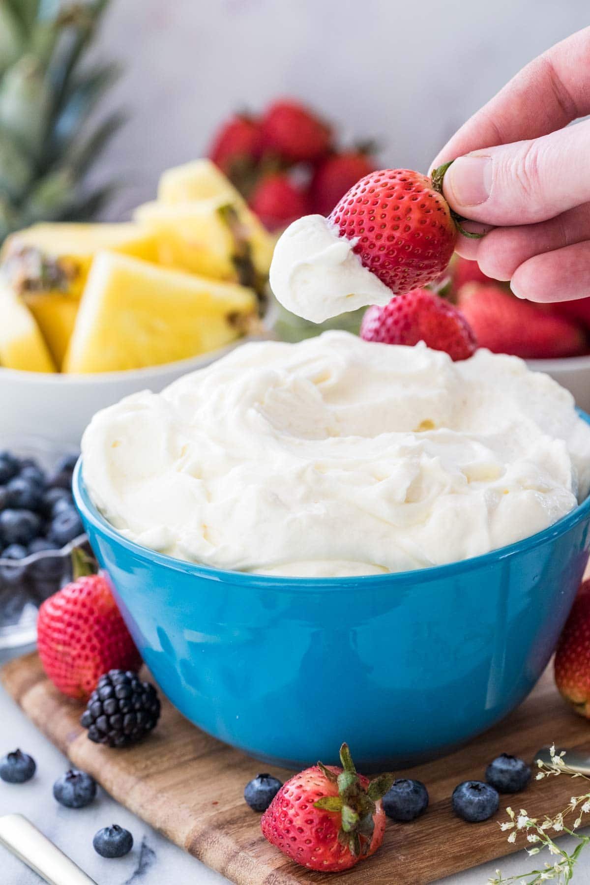 Strawberry being dipped in fruit dip surrounded by other fruit.