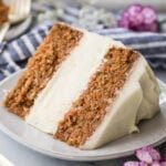 slice of carrot cake cheesecake frosted with cream cheese icing on a white plate