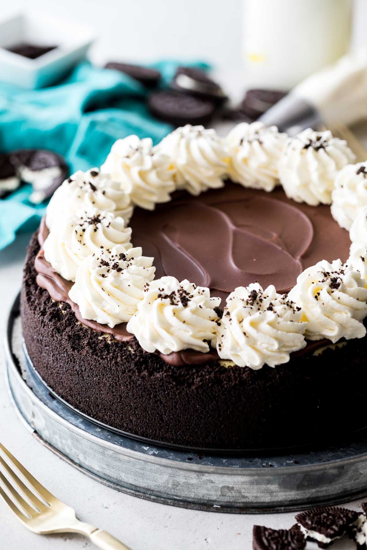 whole cheesecake with an oreo crust, chocolate ganache top, and ring of whipped cream topped with crushed oreos