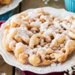 golden brown funnel cake dusted with powdered sugar on a white plate