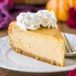 Slice of pumpkin cheesecake topped with cinnamon whipped cream on a white plate.