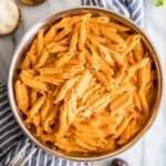 Overhead view of a skillet of penne alla vodka topped with parmesan and fresh basil.