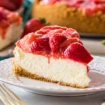 Slice of strawberry cheesecake on a plate with more cheesecake in the background.