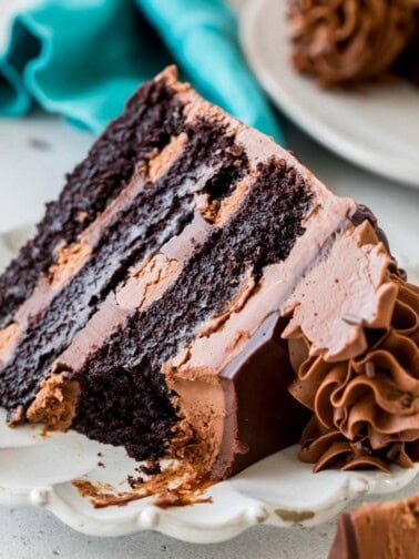Slice of triple chocolate cake missing a bite on a white plate.