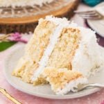 Slice of coconut cake on a plate with a forkful missing