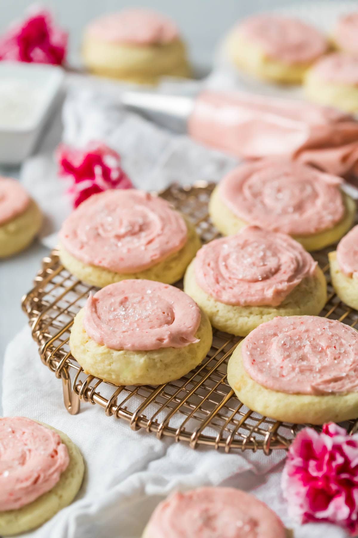 Sour cream cookies topped with a pale pink frosting on a cooling rack.