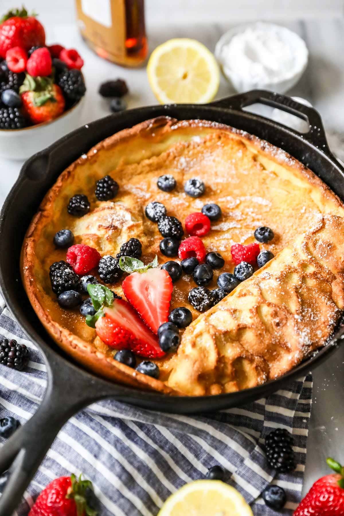 Dutch baby topped with fresh berries and powdered sugar in a cast iron skillet.