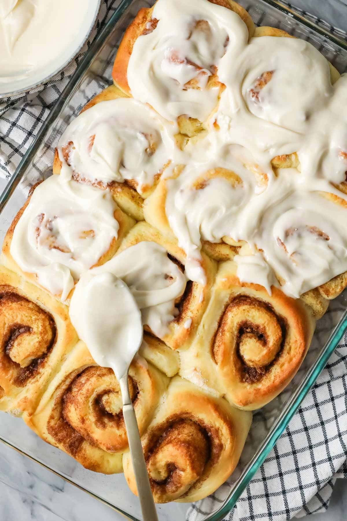 Overhead view of cinnamon roll icing being spread over rolls.