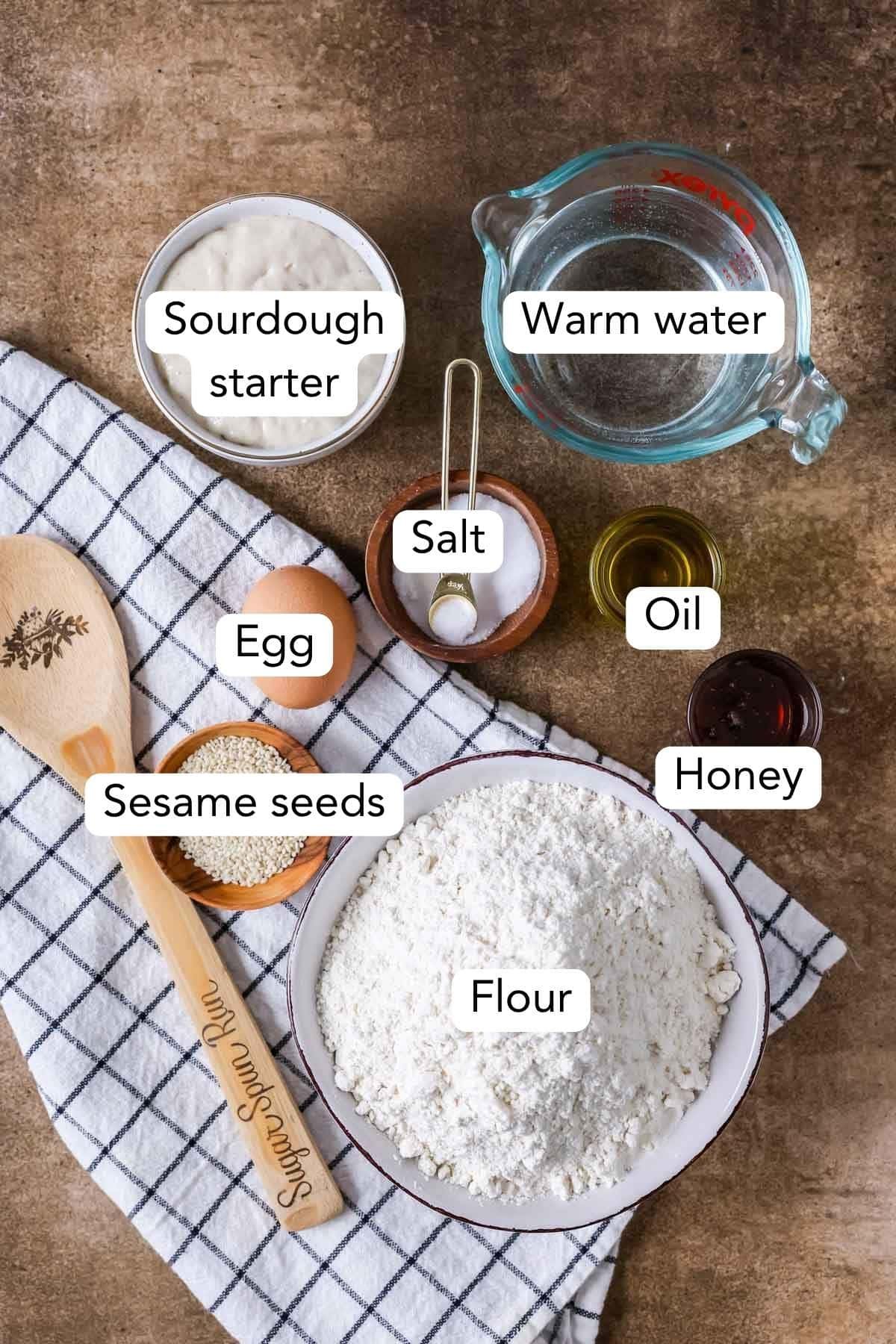 Overhead view of labeled ingredients including bread flour, sesame seeds, sourdough starter, and more.