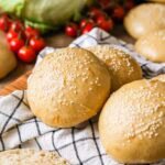 Homemade sourdough burger buns topped with sesame seeds on a kitchen towel.