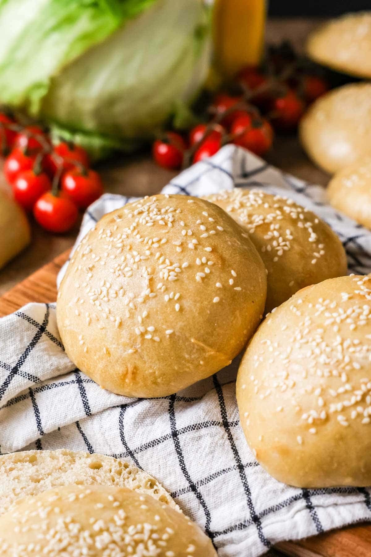 Homemade sourdough burger buns topped with sesame seeds on a kitchen towel.