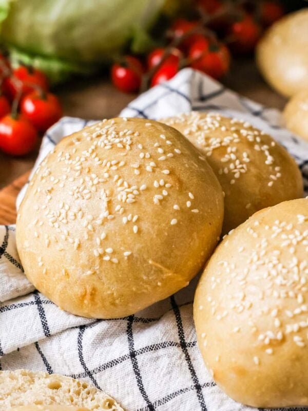 Homemade sourdough burger buns topped with sesame seeds on a kitchen towel.